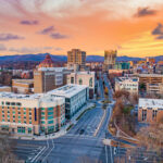 An aerial shot of Asheville, North Carolina, at sunset. Many of the buildings, including Art Deco skyscrapers can be seen, with the Blue Ridge Mountains in the background