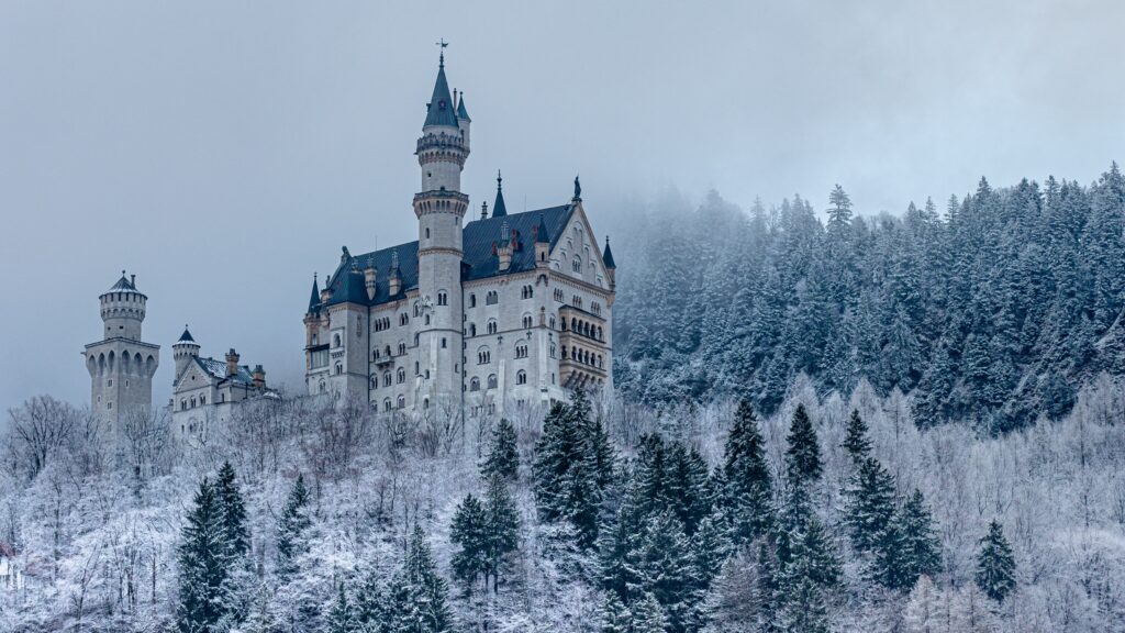 Neuschwanstein Castle near Munich in Germany can be seen in the winter can be seen from below. The forest that surrounds it is covered in snow