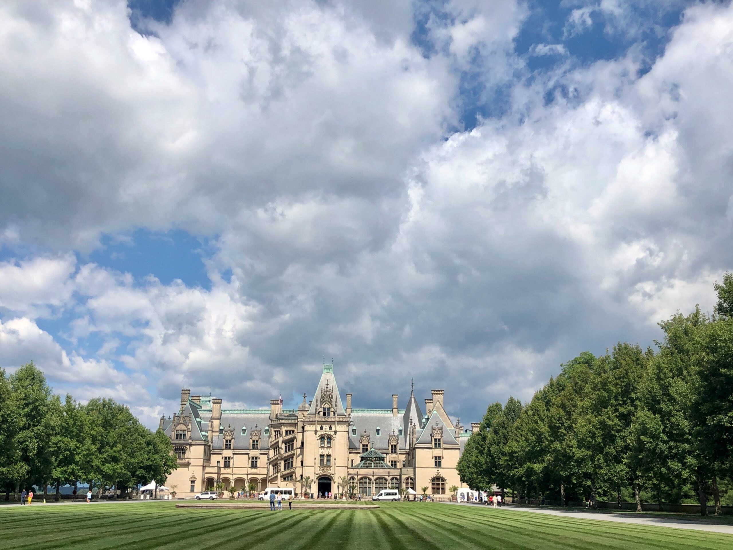 Biltmore Estate in Asheville can be seen from the lawn under fluffy clouds and blue skies