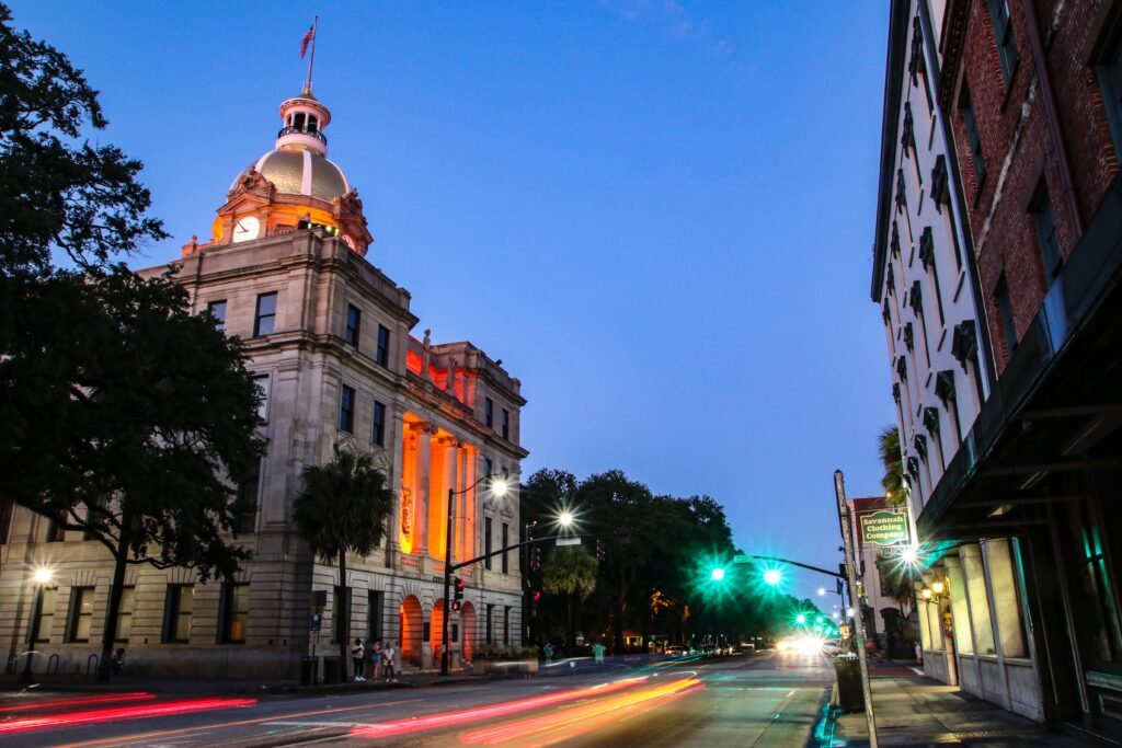 The Savannah City Hall can be seen lit up at dusk. Streaks of car tail lights shoot past in the long exposure photograph