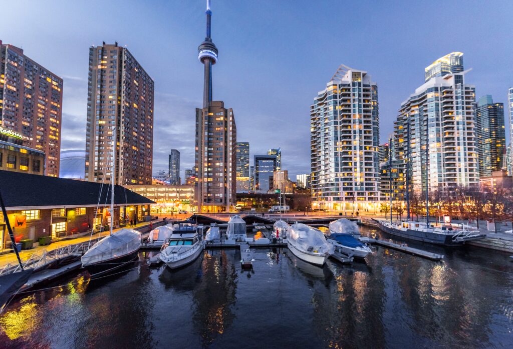The Toronto skyline lit up at night as seen from Queens Quay West. There are a number of pleasure boats docked in the foreground