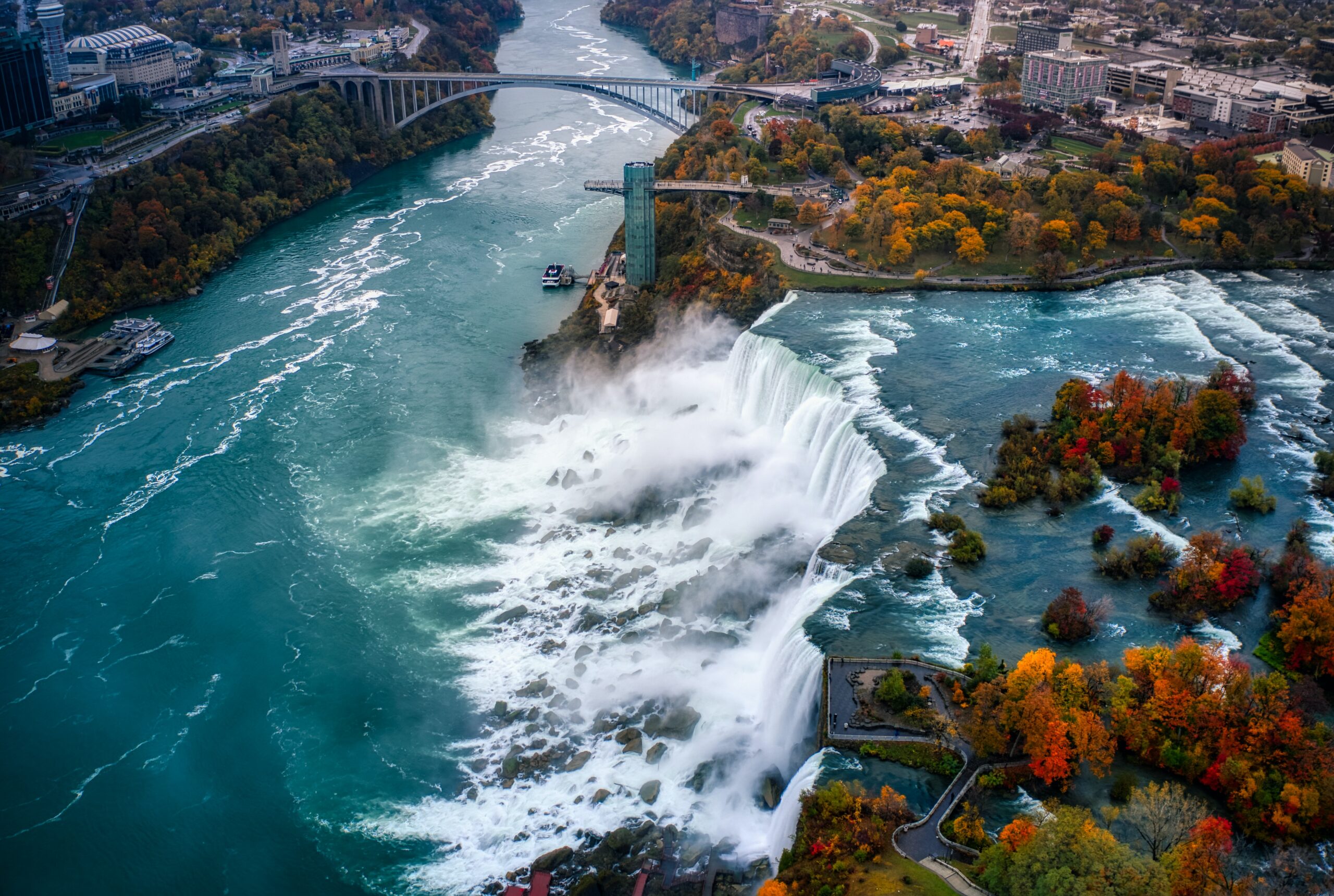 Water tumbles of the top of Niagara Falls in the autumn. The picture is an aerial shot and the falls are surrounded by fall foliage