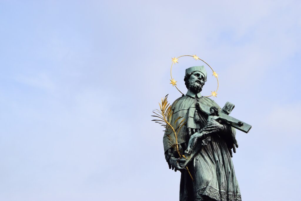A statue of St John of Nepomuk on the Charles Bridge in Prague. He holds a crucifix and a golden quill. Around his head is a golden halo