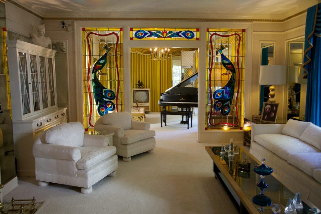Elvis' living room in Graceland. There are plush sofas and chairs, stained glass windows and a grand piano with its lid up — David Brossard / Flickr