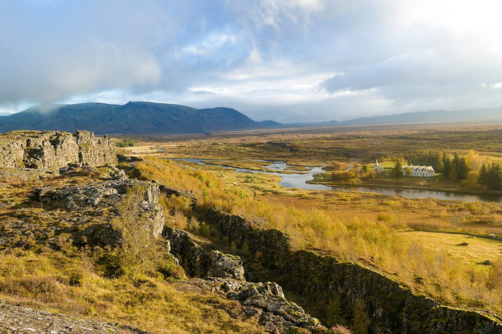 The Mid-Atlantic Rift in Iceland. There are some houses in the distance and body of water surrounded by grass