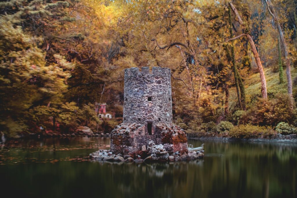 A small stone tower in the gardens of Pena Palace. It stands in the middle of a lake surround by fall foliage